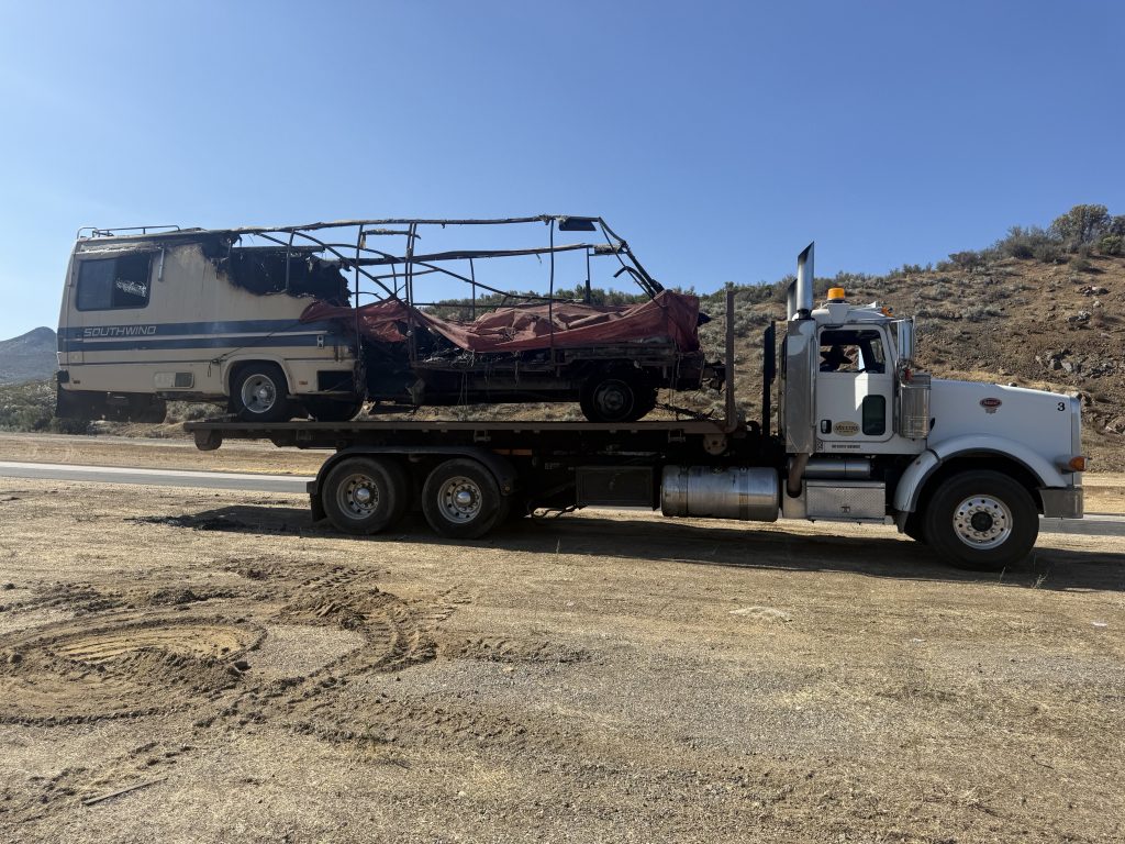 A heavy-duty tow in progress involving a large, burned-out RV in Jacumba Hot Springs.